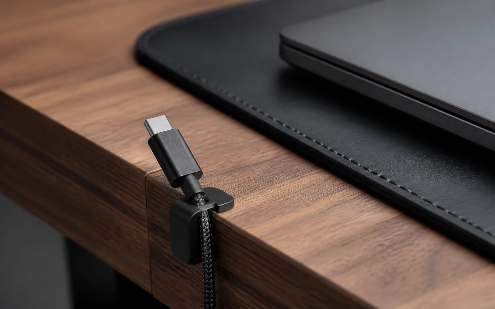 کابل USB-C پارک‌شده در گیره لبه میز کنار لپ‌تاپ و دسک‌پد مشکی